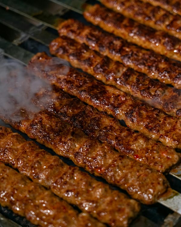 Close-up of spicy Persian Tabrizi-style Koobideh kababs grilling on flat skewers, steam rising